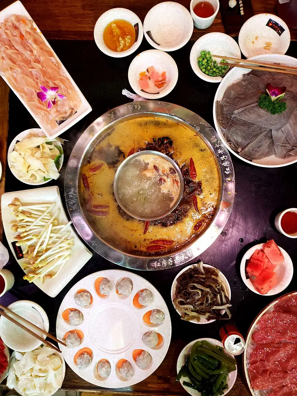 A divided Chongqing hotpot with spicy broth, a central soup section and plates of ingredients